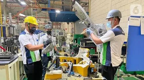 Operator produksi bekerja di area manufaktur dengan mesin produksi